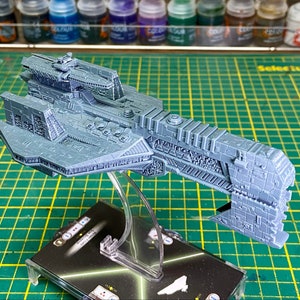May include: A gray, detailed, plastic model of a spaceship, sitting on a clear plastic stand. The spaceship is on a black and white card with green lines.