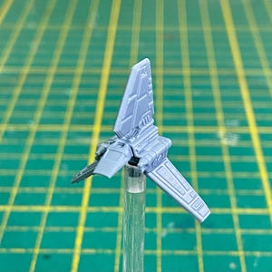 以下が含まれることがあります： スターウォーズのTIEファイター宇宙船のグレーのプラスチックモデル。モデルは透明なプラスチックスタンドの上にあります。