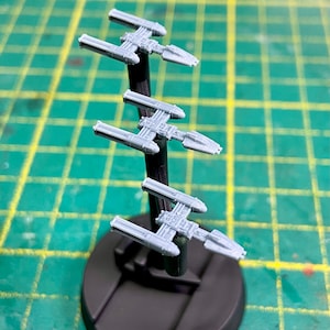Op de afbeelding: Drie grijze plastic model ruimteschepen op een zwarte standaard. De ruimteschepen staan in een rij, waarbij de bovenste het verst van de kijker af staat. De ruimteschepen zijn allemaal in dezelfde richting gericht.