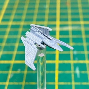 May include: A gray plastic miniature spaceship with a pointed nose and two wings. The spaceship is mounted on a clear plastic rod.