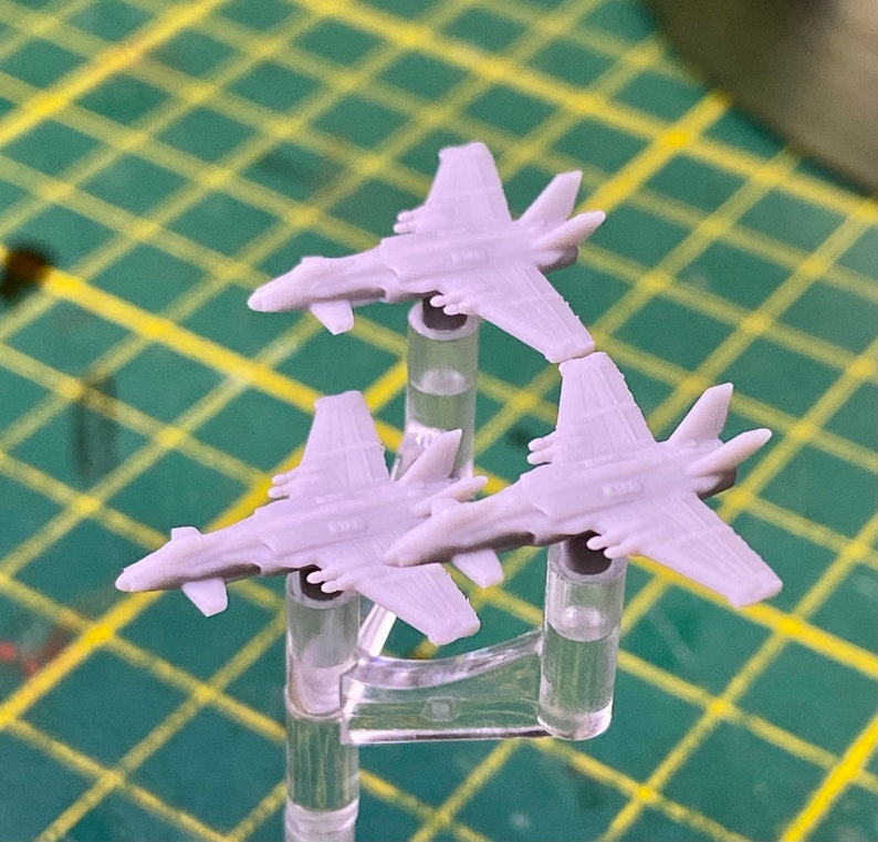 Puede incluir: Tres aviones modelo de pl&aacute;stico gris en soportes de pl&aacute;stico transparente. Los aviones est&aacute;n en formaci&oacute;n con las alas de los aviones apuntando hacia el espectador.