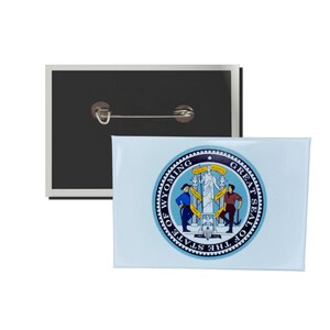 May include: A blue and white button with the Great Seal of the State of Wyoming. The seal features a woman standing on a pedestal with two men standing on either side of her. The seal is surrounded by a blue circle with the words "Great Seal of the State of Wyoming" in gold lettering.
