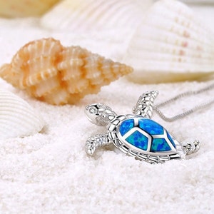 Puede incluir: Un collar con un colgante de tortuga de plata con una incrustación de ópalo azul. La tortuga es un símbolo popular de buena suerte y longevidad.
