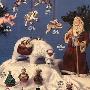 以下が含まれることがあります： クリスマスの飾りを特集したカタログページ。オーナメントには、サンタクロースのフィギュア、星型の装飾品、動物の置物などがあります。南西をテーマにした村や、プレゼントの袋を持ったホッキョクグマもあります。「'Tis the Season」というテキストが上部にあります。