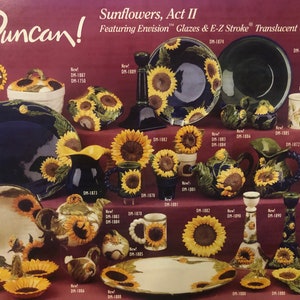 May include: A collection of ceramic sunflower-themed kitchenware, including plates, bowls, mugs, pitchers, and candle holders. The items are decorated with sunflowers in various shades of yellow and brown, with green leaves and stems. The text "Duncan!" and "Sunflowers, Act II" is visible at the top of the image.