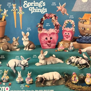 Puede incluir: Una colección de decoraciones de Pascua de cerámica, que incluyen conejos, pollitos, un cerdo, un cordero y una cesta llena de flores. Las decoraciones están pintadas en colores pastel y presentan detalles caprichosos. La imagen también incluye un arca de cerámica con animales a bordo, un gallo y una maceta de zanahorias con conejos.