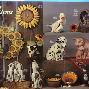 May include: A catalogue page showcasing rustic home decorations. It features a sunflower clock, a wreath with sunflowers, and animal figurines including ducks, rabbits, dogs, pigs, and cats. The text "Rustic Gems" is displayed at the top.