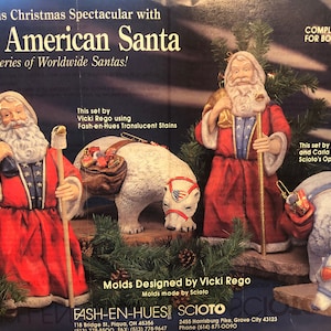 Puede incluir: El conjunto de adornos navideños American Santa incluye una figura de Papá Noel con una túnica roja y azul, sosteniendo un bastón y una bolsa de regalos. El conjunto también incluye un oso polar con una silla de montar roja, blanca y azul. El conjunto de adornos está hecho por Sciato y diseñado por Vicki Rego.