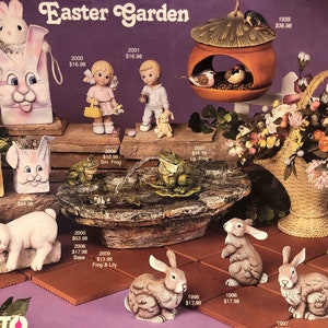 Può includere: Una collezione di statuine da giardino pasquale in ceramica, tra cui una borsa a forma di coniglio, una casetta per uccelli, una fontana di rane e un coniglietto addormentato. Le statuine sono dipinte in colori pastello e presentano dettagli realistici.