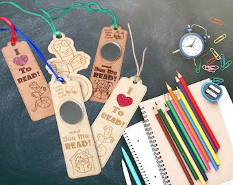 May include: Wooden bookmarks with the text "I TO READ!" and "and See me READ!" are displayed. The bookmarks feature illustrations of a worm reading a book and a child reading. A blue alarm clock, colored pencils, and a notebook are also visible.