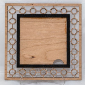May include: A wooden picture frame with a geometric pattern around the edge. The frame has a black border and a cutout in the center.