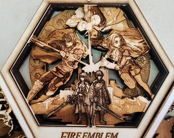 Puede incluir: Una caja hexagonal de madera con un diseño recortado que presenta personajes del videojuego Fire Emblem: Three Houses. La caja tiene un acabado de madera marrón y el texto "Fire Emblem Three Houses" está impreso en la parte delantera.