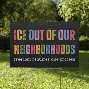 May include: A black sign with the text "ICE OUT OF OUR NEIGHBORHOODS" in colorful letters. The phrase "freedom requires due process" is below the main text. The sign is placed in a grassy yard.