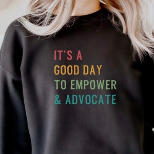 May include: Black sweatshirt with the text "It's a good day to empower & advocate" in rainbow colours.