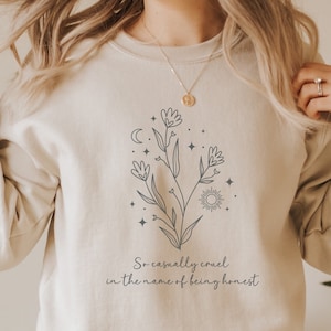 May include: A beige sweatshirt with a floral design and the text "So casually cruel in the name of being honest".