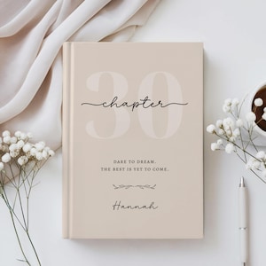May include: A beige hardcover book featuring the large text "30" in the background, with the word "chapter" in cursive script above the text "DARE TO DREAM. THE BEST IS YET TO COME." and the name "Hannah" printed in a cursive font at the bottom.
