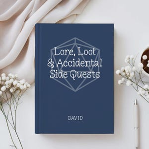 May include: A dark blue hardcover book with white text that reads Lore, Loot & Accidental Side Quests above a geometric icosahedron outline. The name DAVID is printed in white near the bottom center of the front cover of the book.