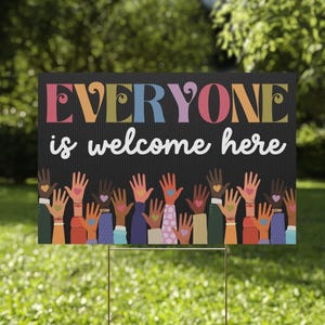 May include: A rectangular yard sign with a black background featuring vertical pinstripes. The text EVERYONE is written in large, colorful, stylized letters, followed by the white script text is welcome here. Below are many raised hands.