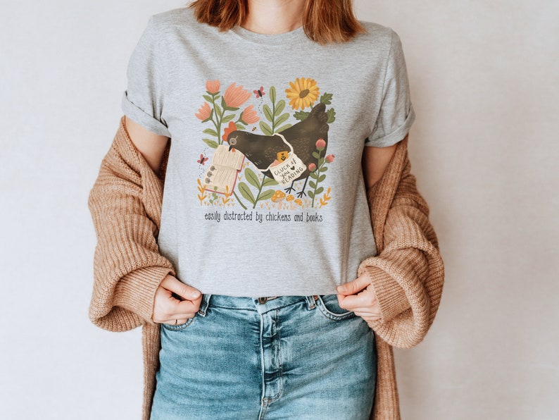 May include: Gray t-shirt with a black chicken reading a book. The book says "Such a Luck if You're Reading". The shirt has a floral design and the text "easily distracted by chickens and books".