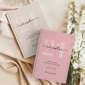 May include: Two hardcover journals, one in beige and one in dusty rose, featuring the large number 21, the word chapter in script, and the text Dare to dream. The best is yet to come. Each journal is personalized with the name Hannah in script.