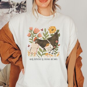May include: White sweatshirt with a graphic of a chicken holding a book with the text "Cluck You I Love Reading" and the text "easily distracted by chickens and books".