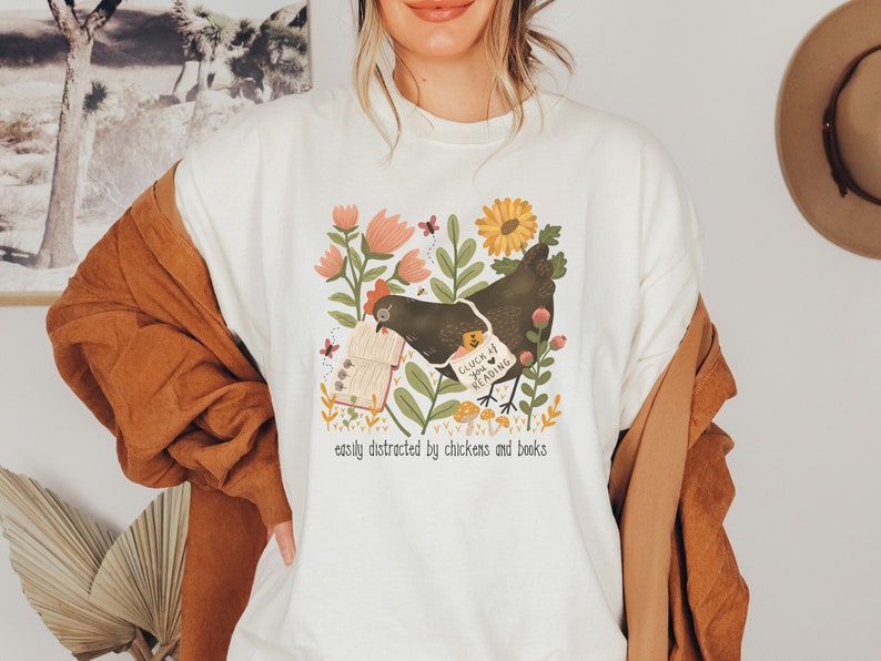 May include: White sweatshirt with a graphic of a chicken holding a book with the text "Cluck You I Love Reading" and the text "easily distracted by chickens and books".