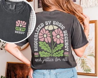 May include: Dark gray t-shirt with a floral design and the text "RADICALIZED BY BASIC DECENCY and justice for all" on the back. The front of the shirt has the word "RESIST" with a floral design. The shirt is a comfortable, casual style.