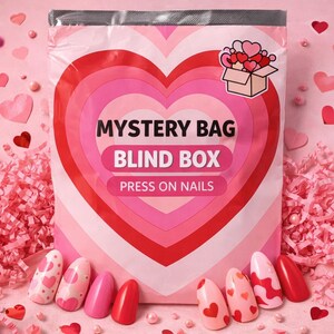 May include: A pink and red heart-themed mystery bag labeled "MYSTERY BAG BLIND BOX PRESS ON NAILS." The bag is surrounded by pink confetti, hearts, and several press-on nails with heart designs. The nails are various shades of pink and red.