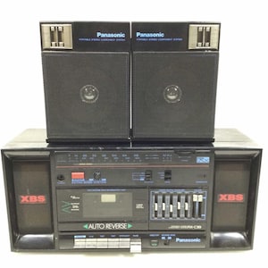 May include: Black Panasonic portable stereo component system with two detachable speakers. The stereo features an AM/FM radio, cassette player, and equalizer. The speakers have a mesh grill and the stereo has the text "XBS" and "Extra Bass System".