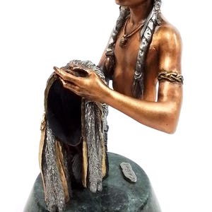 May include: Bronze sculpture of a Native American woman with long braided hair, holding a feathered headdress. The sculpture is on a green marble base with the artist's signature.