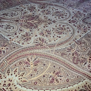 May include: Close-up of a fabric with a paisley pattern in shades of gray, blue, and burgundy. The fabric has a detailed design with floral and curved elements. The text "RALPH LAUREN HOME" is visible at the bottom.