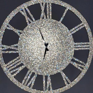 Puede incluir: Un reloj grande, redondo y plateado con números romanos. La esfera del reloj está cubierta de purpurina iridiscente.