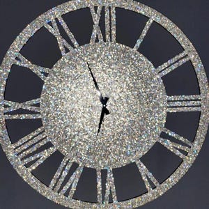 Può includere: Un grande orologio rotondo argentato con numeri romani. Il quadrante dell'orologio è ricoperto di glitter iridescente.