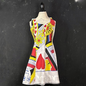 May include: A sleeveless dress with a playing card design. The dress features a white background with red, yellow, and black playing card symbols. The dress is displayed on a mannequin.