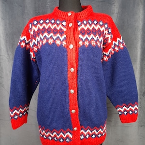 May include: A long-sleeve knit cardigan featuring a deep blue base with vibrant red trim along the collar, cuffs, and hem. The garment displays a repeating geometric pattern in red, white, and blue across the chest, shoulders, and sleeves, secured by silver-toned metal buttons.