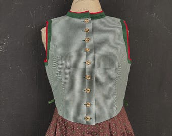 May include: A green and white checkered vest with a high collar and wooden buttons. The vest has red trim and is paired with a brown skirt with white polka dots. The outfit is displayed on a mannequin.