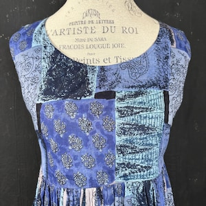 May include: A blue and white sleeveless dress with a patchwork design. The dress has a floral print and a geometric pattern. The dress is made of a lightweight fabric and has a flowy silhouette.