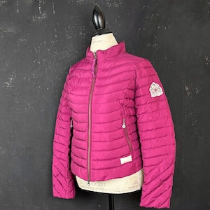 May include: A magenta puffer jacket with a full-length zip, side pockets, and a high collar. The jacket has a logo patch on the upper left sleeve and a small label near the hem. The jacket is displayed on a mannequin.