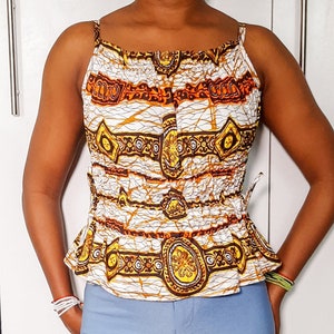 May include: A white sleeveless top with a brown and gold patterned design. The top has a gathered neckline and a cinched waist.