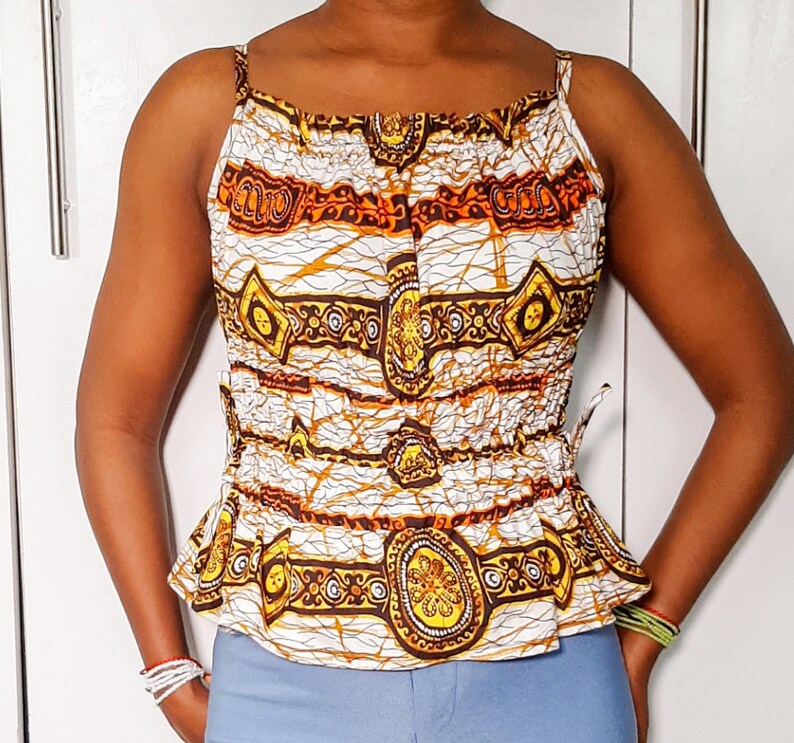 May include: A white sleeveless top with a brown and gold patterned design. The top has a gathered neckline and a cinched waist.