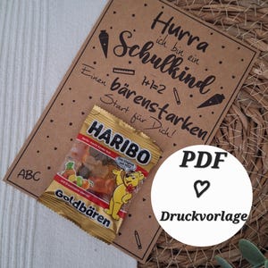 Könnte beinhalten: Eine Karte aus Kraftpapier mit dem Text "Hurra ich bin ein Schulkind" und einer kleinen Tüte Gummibärchen von Haribo Goldbären. Die Karte hat Illustrationen von Karotten und Bleistiften.