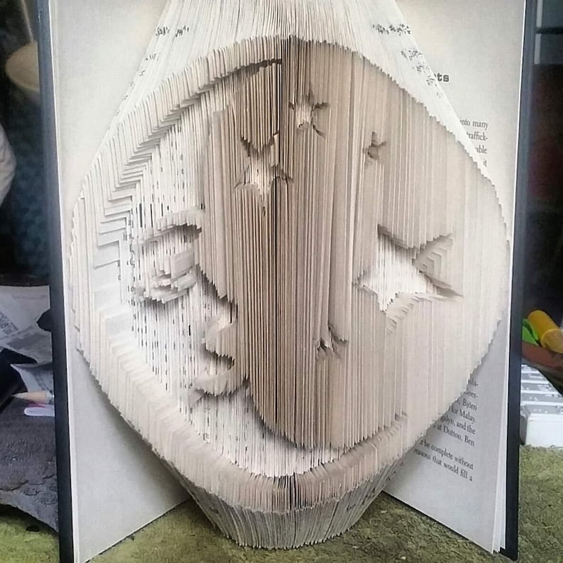 Pu&ograve; includere: Un libro piegato in una scultura tridimensionale di un uccello. La scultura &egrave; realizzata dalle pagine di un libro, e le pagine sono piegate e sovrapposte per creare la forma dell'uccello.