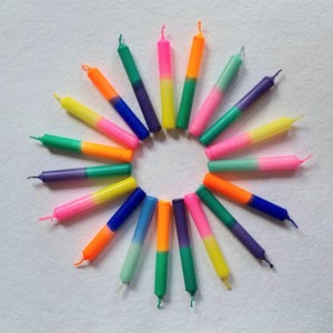 Könnte beinhalten: Ein Kreis aus 18 bunten Geburtstagskerzen mit zweifarbigen Farben. Die Kerzen sind in einem Kreis angeordnet, wobei die Spitzen nach außen zeigen. Die Kerzen sind in verschiedenen Farben, darunter rosa, grün, blau, gelb und orange.