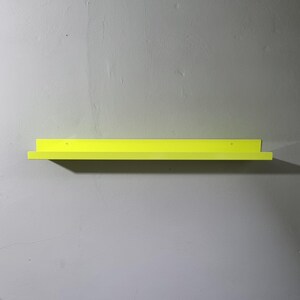 May include: A bright yellow metal shelf mounted on a wall. The shelf is simple and modern in design.
