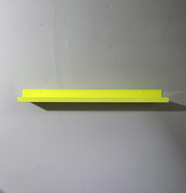May include: A bright yellow metal shelf mounted on a wall. The shelf is simple and modern in design.