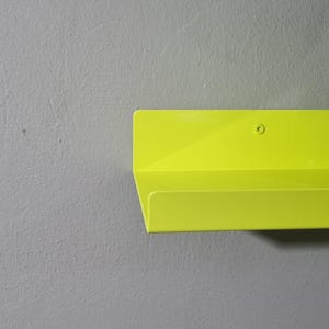 May include: A bright yellow metal shelf with a single screw visible on the top. The shelf is mounted on a gray wall.
