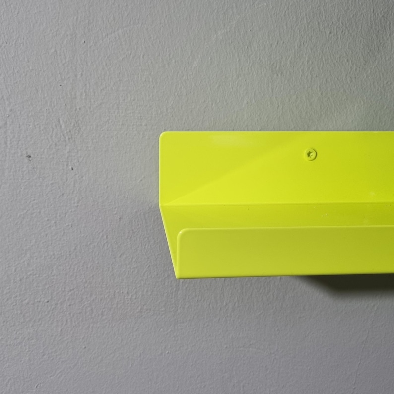 May include: A bright yellow metal shelf with a single screw visible on the top. The shelf is mounted on a gray wall.