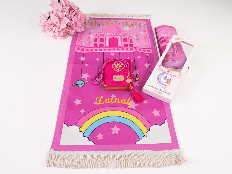 Puede incluir: Alfombra de oraci&oacute;n rosa con un arco&iacute;ris, estrellas y un dise&ntilde;o de mezquita. Viene con un libro de oraciones a juego, cuentas de oraci&oacute;n y una caja de regalo que dice "Ramadan Mubarak Zainab".