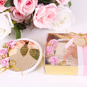 Peut inclure: Une bo&icirc;te ronde blanche avec un design de corde dor&eacute;e et un motif floral rose et or. La bo&icirc;te contient un miroir rond avec une inscription dor&eacute;e en arabe. La bo&icirc;te est attach&eacute;e avec un ruban rose et une &eacute;tiquette dor&eacute;e qui dit "Muhammad Eid Mubarak".