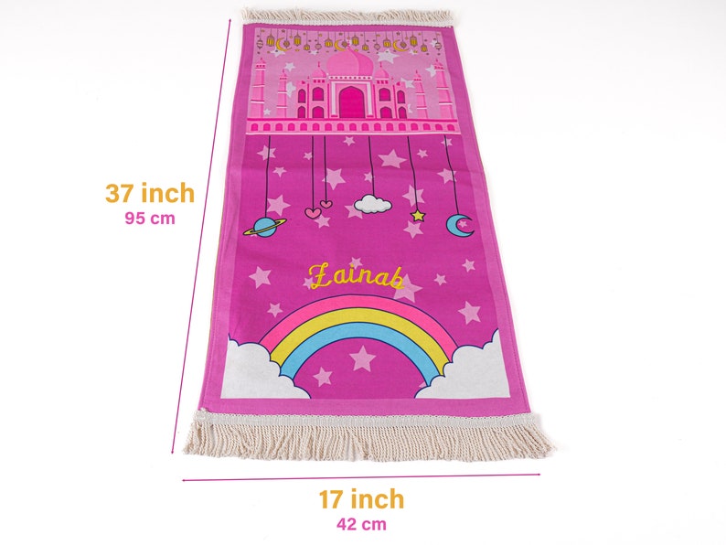 Puede incluir: Alfombra de oraci&oacute;n rosa con un arco&iacute;ris, estrellas y el nombre "Lainab" impreso en ella. La alfombra mide 95 cm por 42 cm.
